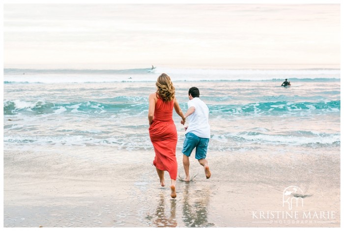 Couple running into ocean | Swamis Beach Sunset Engagement Photo | Encinitas Wedding and Engagement Photographer | Kristine Marie Photography | © www.kristinemariephotography.com